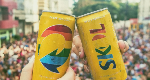 Duas latas Skol personalizadas, com a logo nas cores da bandeira lgbt